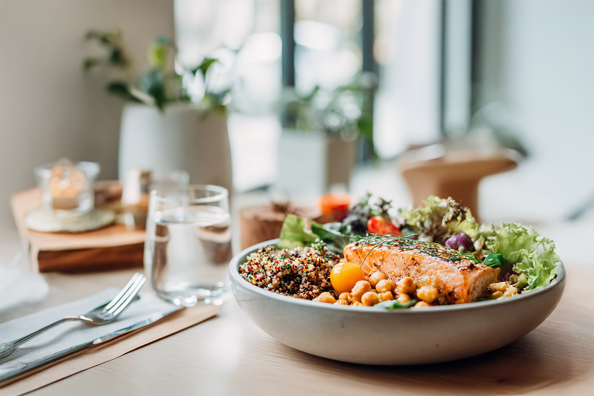 Sättigende Bowl mit Lachs, Kichererbsen, Quinoa und Salat neben einem Glas Wasser auf einem Holztisch
