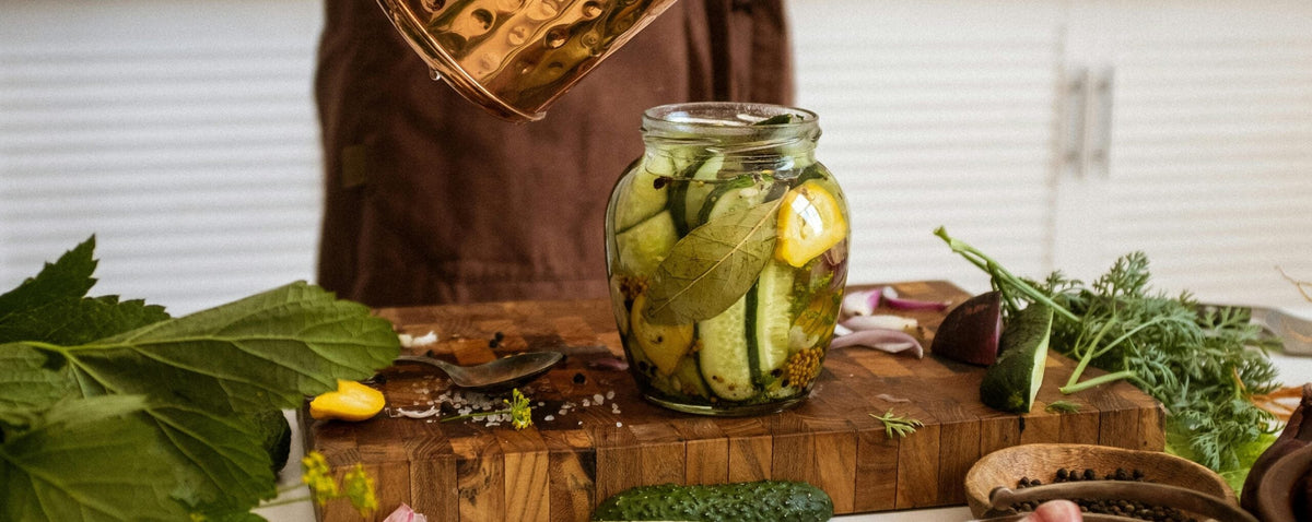 Einmachglas mit fermentierten Gurken, Kräutern und Gemüse auf einem Holzbrett