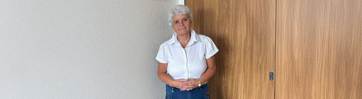 Susanne (65) nach ihrer Gewichtsabnahme mit Precon in weißer Bluse vor einer Holzwand