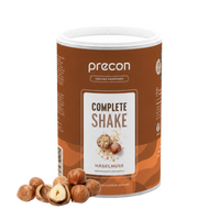 Ein Behälter mit „Anona GmbH Complete Shake Haselnuss“ steht aufrecht, davor sind auf weißem Hintergrund mehrere ganze und geschälte Haselnüsse angeordnet.